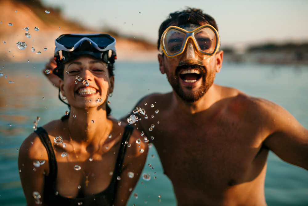 couple in water wearing goggles having just come up from snorkeling 